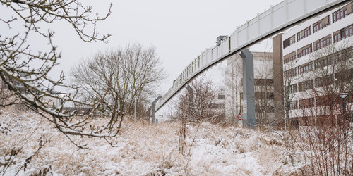 Verschneiter Nordcampus mit einem Gebäude, der H-Bahn-Strecke und Bäumen