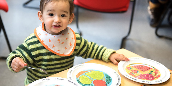 Children plates_01 Toddler playing with three children's plates from the dining hall and sitting at a table.