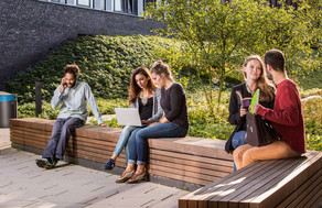 Studierende sitzen auf einer Sitzgruppe hinter dem neuen Physikgebäude