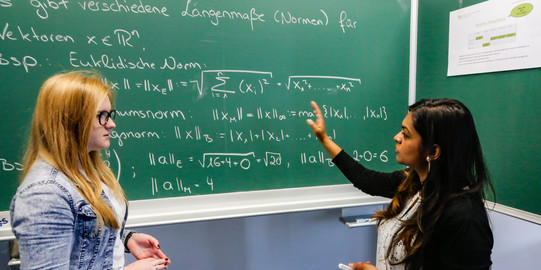 Two students are standing in front of a blackboard.