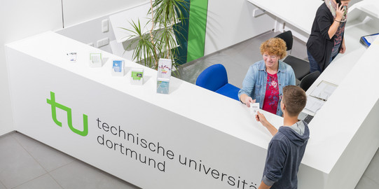 Academic Advice A person from the Academic Advice team is handing over a queue ticket to a student.