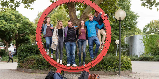 Studierende stehen gemeinsam in einem roten Zahnrad.