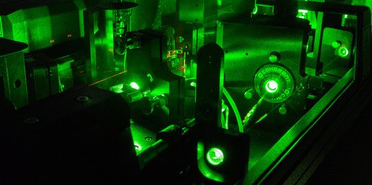 Eine Detailaufnahme eines Lasers im Labor in dunkel grünen Farben.