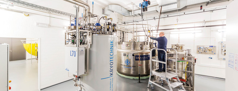 Ein Labor mit einem großen weißen Behälter für Kyrotechnik und einem Metallbehälter, ein Mann steht auf einer Leiter.